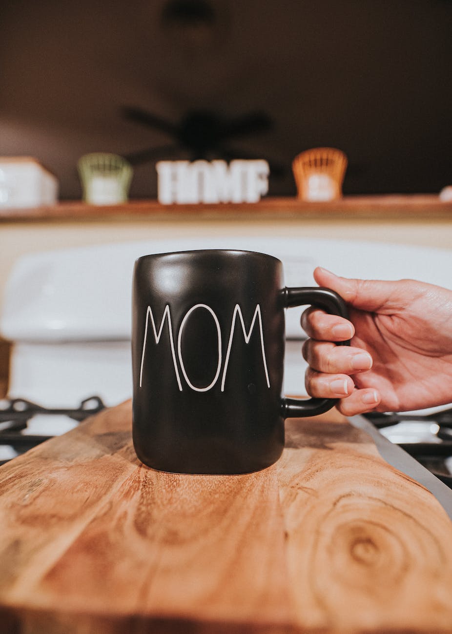 crop faceless person taking black mug with word mom